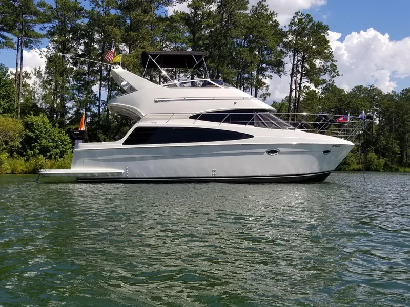 The Image of 2004 Carver 360 Sport Sedan yacht on a serene lake, surrounded by lush trees. - 1