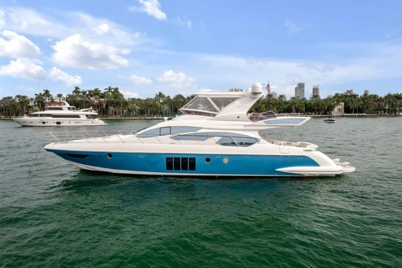 The Image of 2014 Azimut 64 Flybridge yacht on calm water, with a scenic coastal backdrop. - 0