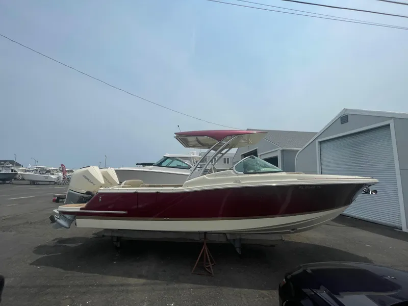 Slide: The Image of 2023 Chris-Craft Calypso 28 boat with red hull, parked outdoors near storage units. - 8