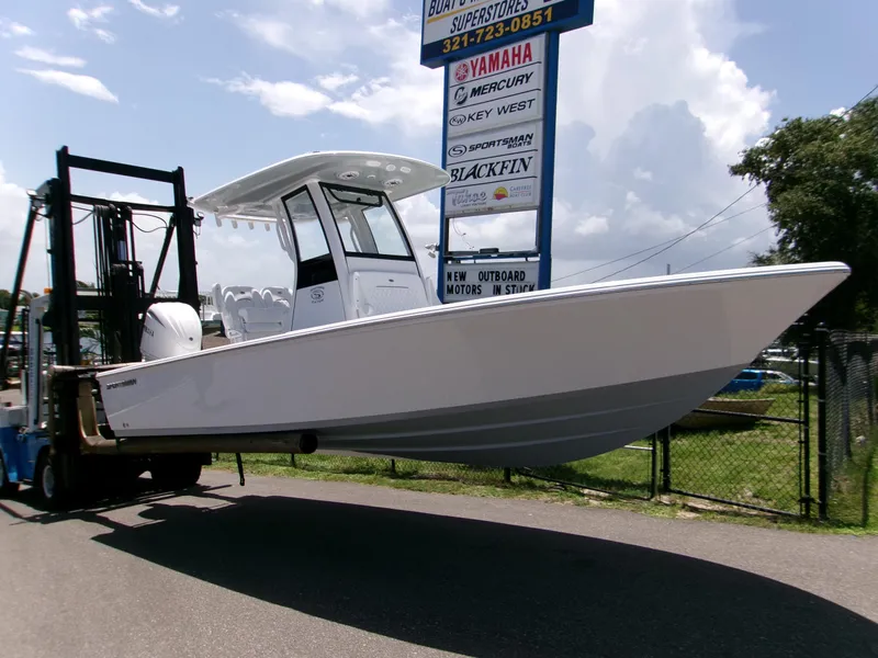 The Image of 2025 Sportsman Masters 247OE Bay Boat on forklift, displayed outdoors near dealership signs. - 0