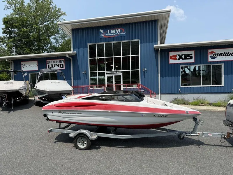 The Image of 2013 Crownline 185 SS boat on trailer outside dealership, blue building background. - 0