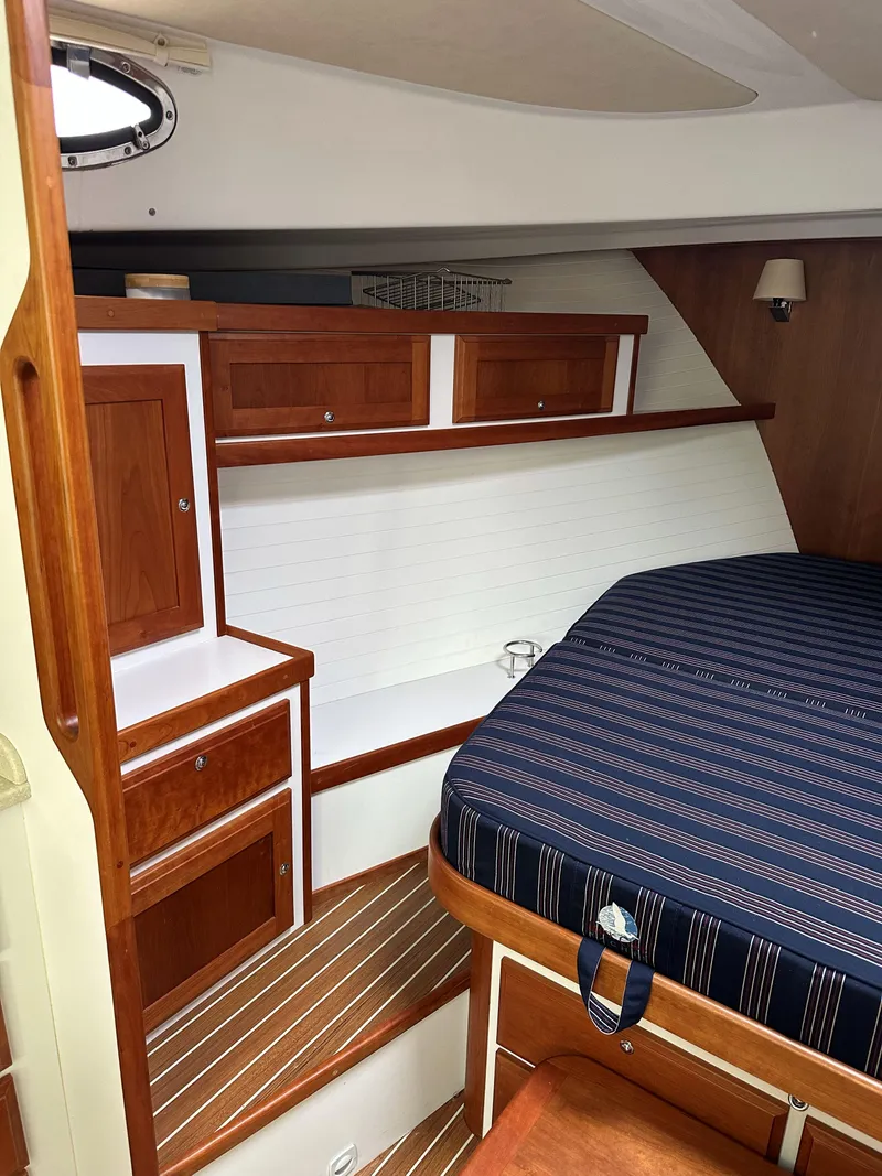 Slide: The Image of 2018 Back Cove Downeast 37 cabin interior with wood cabinetry and striped bedding. - 42