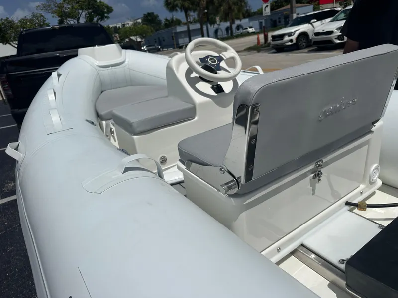 Slide: The Image of 2025 Geniuss 330 Cruiser inflatable boat with white seating and steering wheel, parked outdoors. - 4