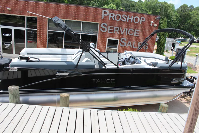Slide: The Image of 2025 Tahoe Pontoon Cascade Quad Lounger at dealership, black exterior, docked near service center. - 5