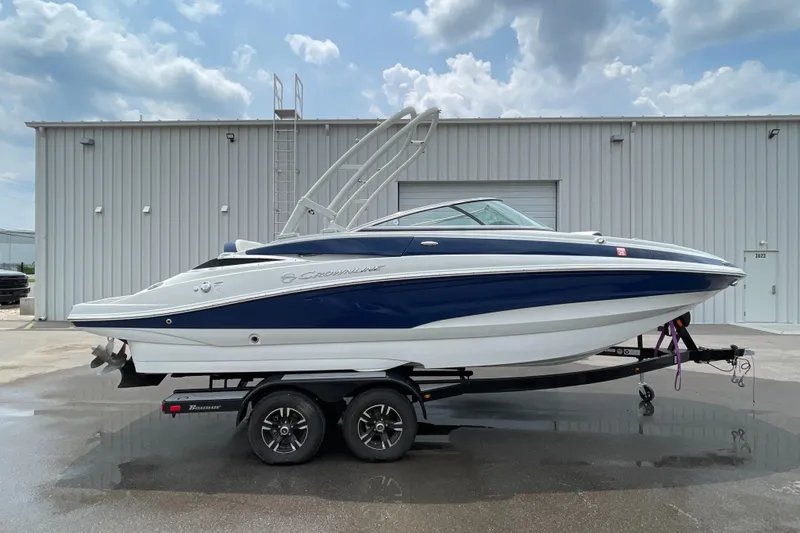 Slide: The Image of 2023 Crownline E235 boat on trailer, parked outside a warehouse under cloudy sky. - 4
