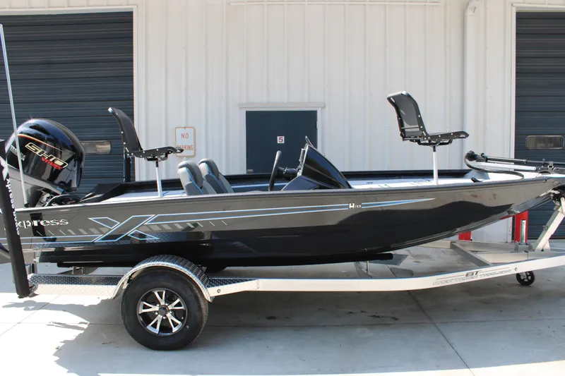 The Image of 2026 Xpress H18C Crappie boat on trailer, black exterior, parked outside a building. - 1