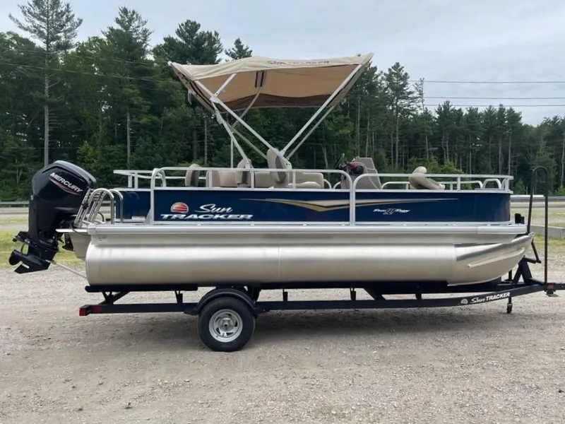 The Image of 2025 Sun Tracker Bass Buggy 18 DLX pontoon boat on trailer, with canopy, in outdoor setting. - 0