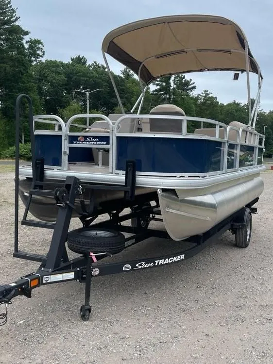 Slide: The Image of 2025 Sun Tracker Bass Buggy 18 DLX pontoon boat on trailer, parked outdoors. - 2
