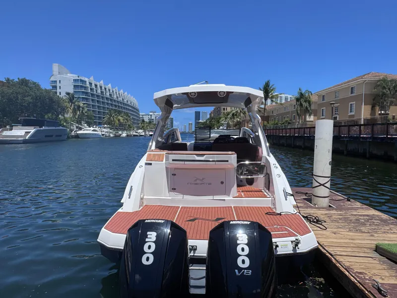 Slide: The Image of 2024 NX Boats 340 Sport Coupe docked on a sunny waterfront. - 2