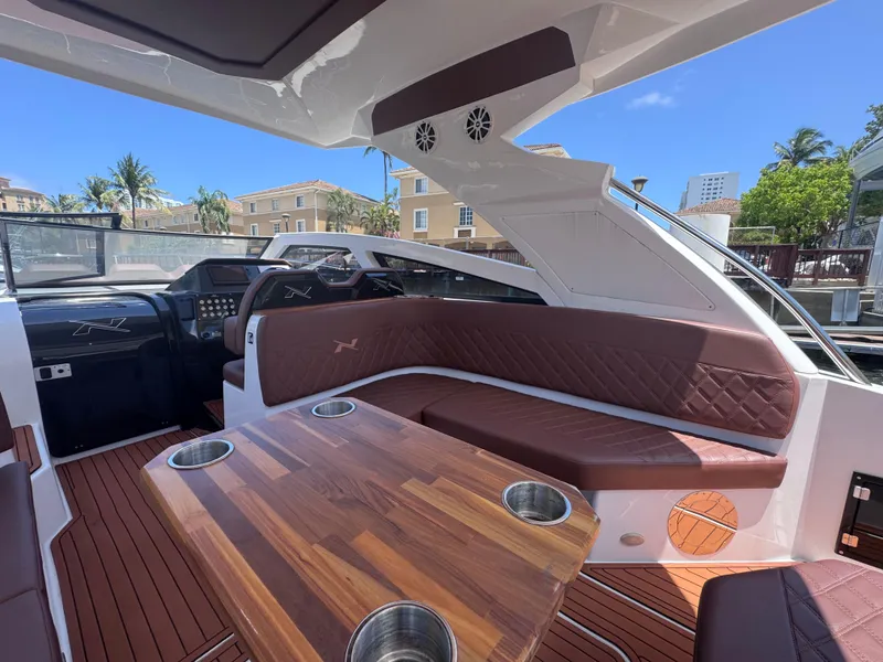 Slide: The Image of 2024 NX Boats 340 Sport Coupe interior with luxurious seating and wooden table, docked under clear skies. - 35