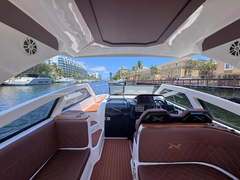 Slide: The Image of 2024 NX Boats 340 Sport Coupe interior with luxurious seating and modern dashboard on a scenic waterway. - 37