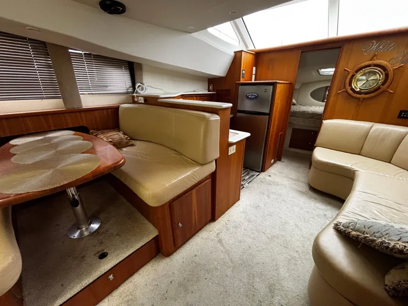 Slide: The Image of 2002 Silverton 330 Sport Bridge interior with beige seating, dining area, and compact kitchen. - 6