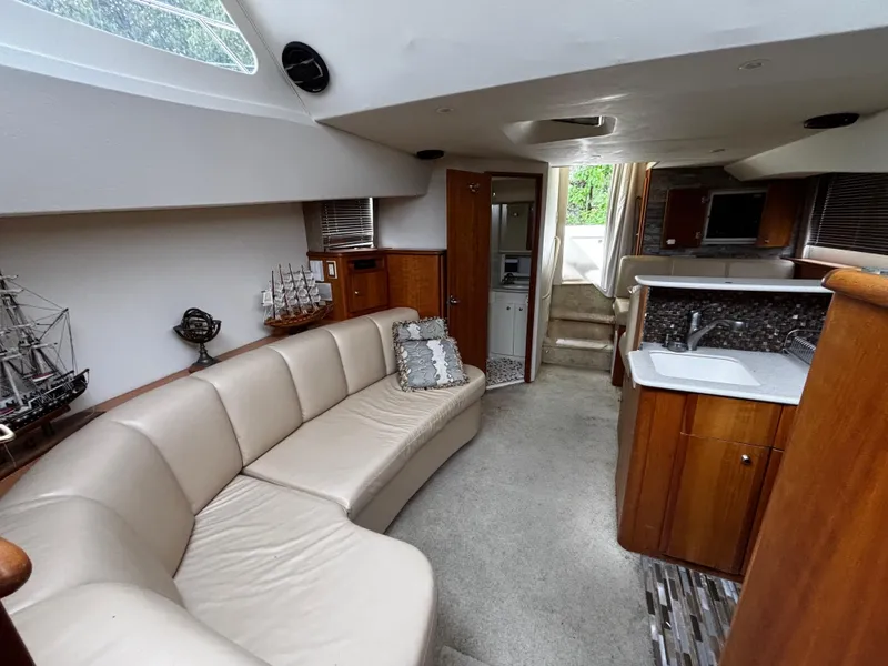 Slide: The Image of 2002 Silverton 330 Sport Bridge interior with beige seating, kitchenette, and nautical decor. - 9