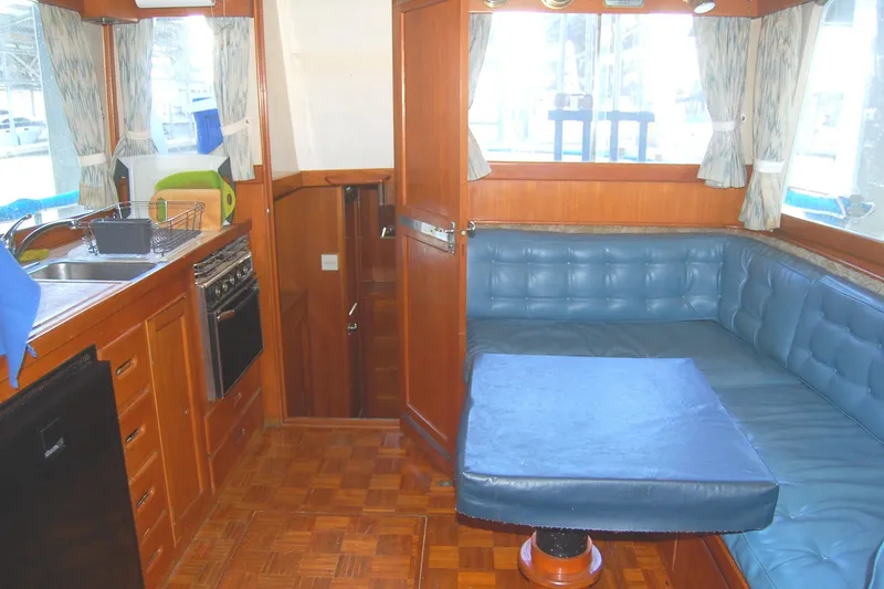 Slide: The Image of 1983 Island Gypsy 36 Quad Cabin interior with blue seating, wooden cabinetry, and kitchen area. - 10