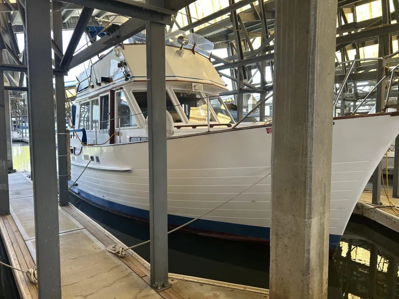 Slide: The Image of 1983 Island Gypsy 36 Quad Cabin docked in a marina, sheltered by metal beams. - 5