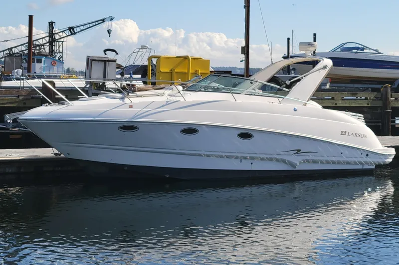 The Image of 2003 Larson 310 boat docked at a marina, with clear skies and industrial background. - 0