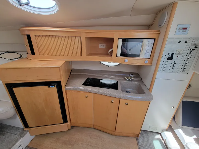 Slide: The Image of 2003 Larson 310 boat interior with kitchenette, featuring microwave, sink, and compact fridge. - 19