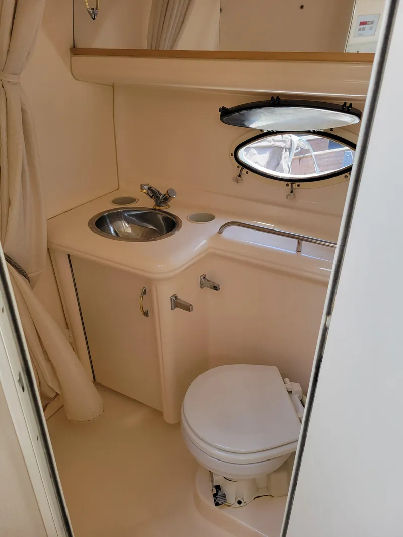 Slide: The Image of 2003 Larson 310 boat bathroom with sink, toilet, and porthole window. - 29