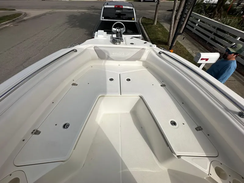 Slide: The Image of 2011 Boston Whaler 220 Outrage boat deck, white, spacious seating, parked on a trailer. - 32
