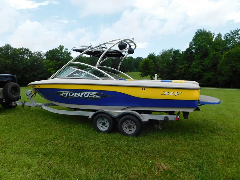 Slide: The Image of 2004 Moomba 23XLV boat with yellow and blue design on a trailer in a grassy field. - 1