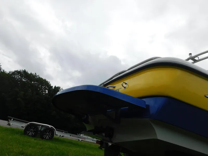 Slide: The Image of 2004 Moomba 23XLV boat with yellow and blue hull on grassy area under cloudy sky. - 5