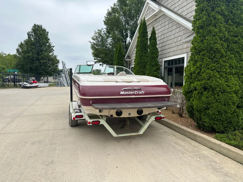 Slide: The Image of 1999 MasterCraft MariStar 210 VRS boat on trailer, parked near a building with greenery. - 3