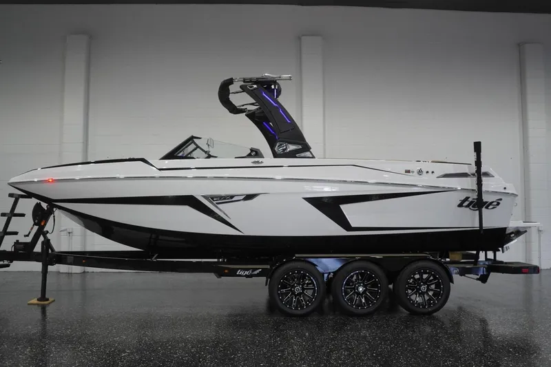 The Image of 2025 Tigé 24RZX boat on trailer in showroom, sleek design, white and black color scheme. - 0
