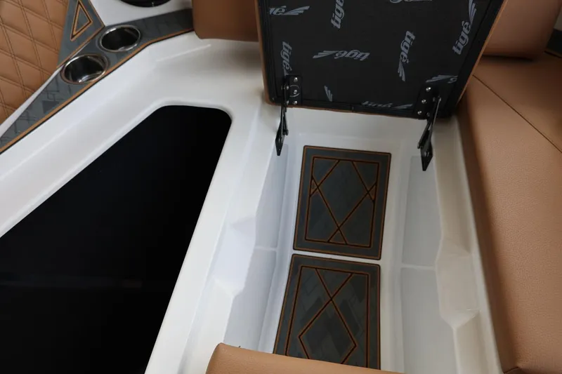 Slide: The Image of 2025 Tigé 24RZX boat interior storage compartment with tan upholstery and cup holders. - 19