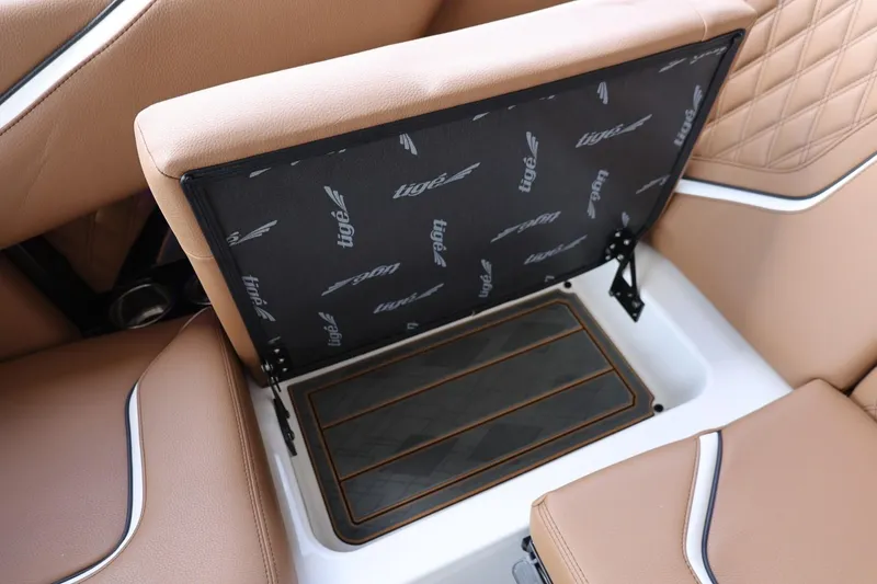 Slide: The Image of 2025 Tigé 24RZX boat interior storage compartment with tan upholstery and branded cover. - 45