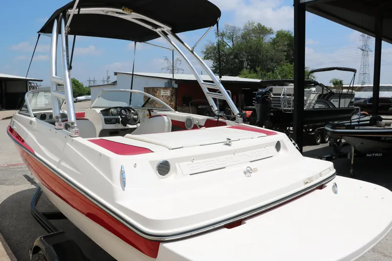 Slide: The Image of 2014 Bayliner 185 BR boat with red accents, parked outdoors under a canopy. - 7