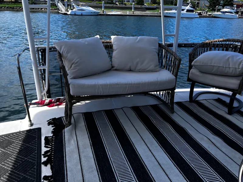 Slide: The Image of Bayliner 4387 Motoryacht 1991 deck with wicker seating and striped rug by the water. - 3