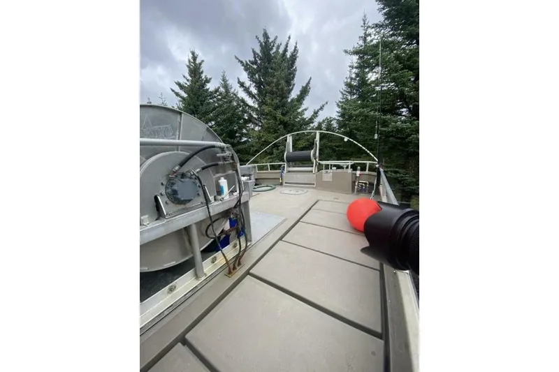 Slide: The Image of Custom Freestyle Marine 32 boat deck with equipment, surrounded by trees, under cloudy sky. - 33