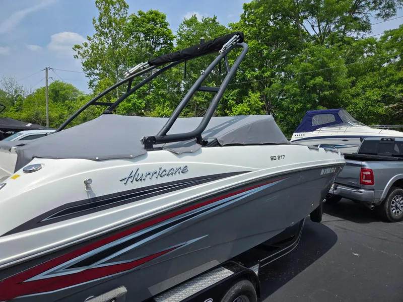 Slide: The Image of 2021 Hurricane SunDeck 217 OB boat on trailer, parked outdoors with trees in background. - 10