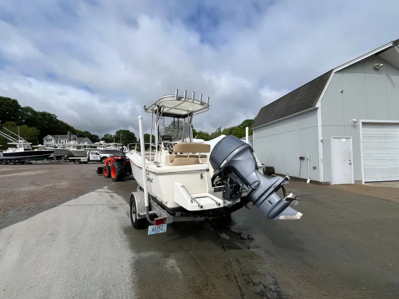 Slide: The Image of 2014 Scout 195 Sportfish boat on trailer, parked near a white building. - 2