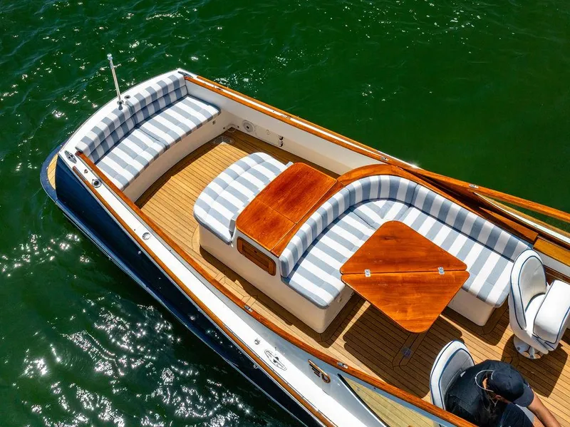 Slide: The Image of 2004 Hinckley Talaria 29 R boat with striped seating and wooden table on green water. - 36