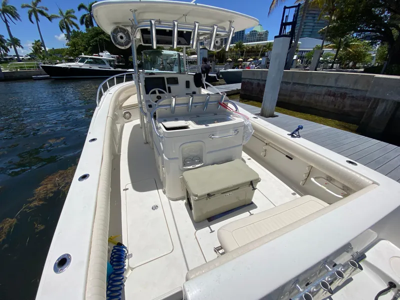 Slide: The Image of 2014 Mako 284 CC boat docked, featuring spacious deck and seating, surrounded by palm trees. - 13