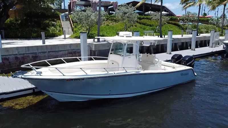 The Image of 2014 Mako 284 CC boat docked by a waterfront with lush greenery. - 2