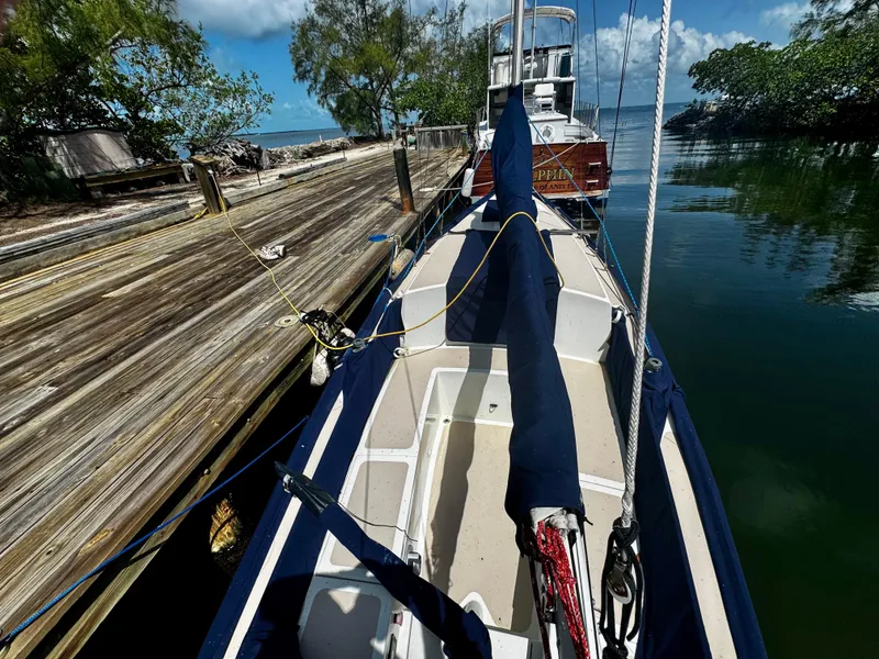 Slide: The Image of 1968 Sailboat 24 docked by a wooden pier, surrounded by calm water and lush greenery. - 7