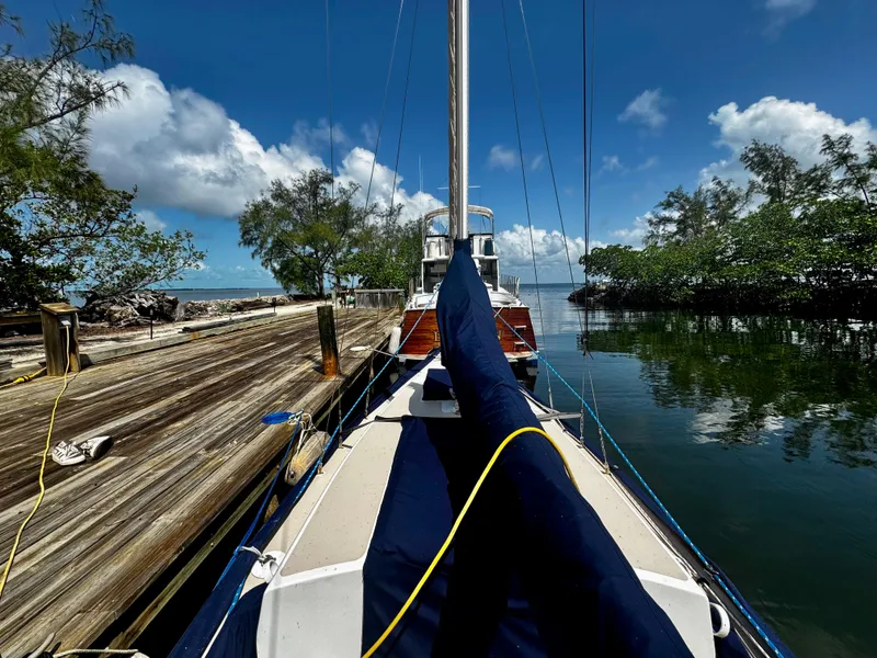 Slide: The Image of 1968 Sailboat 24 docked by a wooden pier, surrounded by lush trees and calm water. - 9