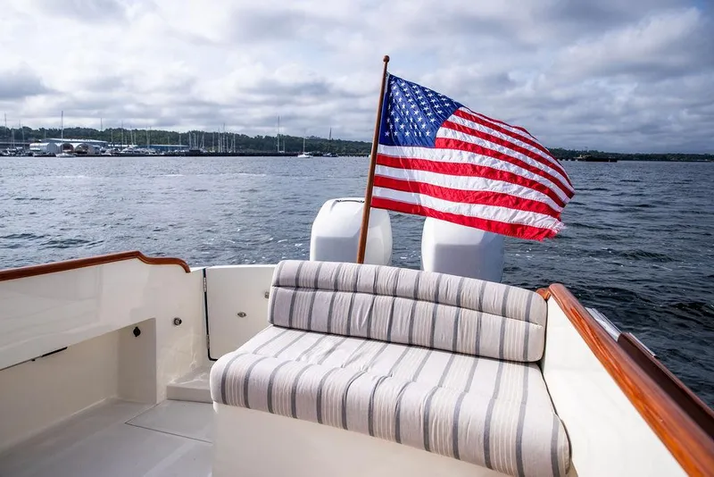Slide: The Image of Hinckley 35 boat (2022) with American flag, striped seating, on a calm lake. - 14