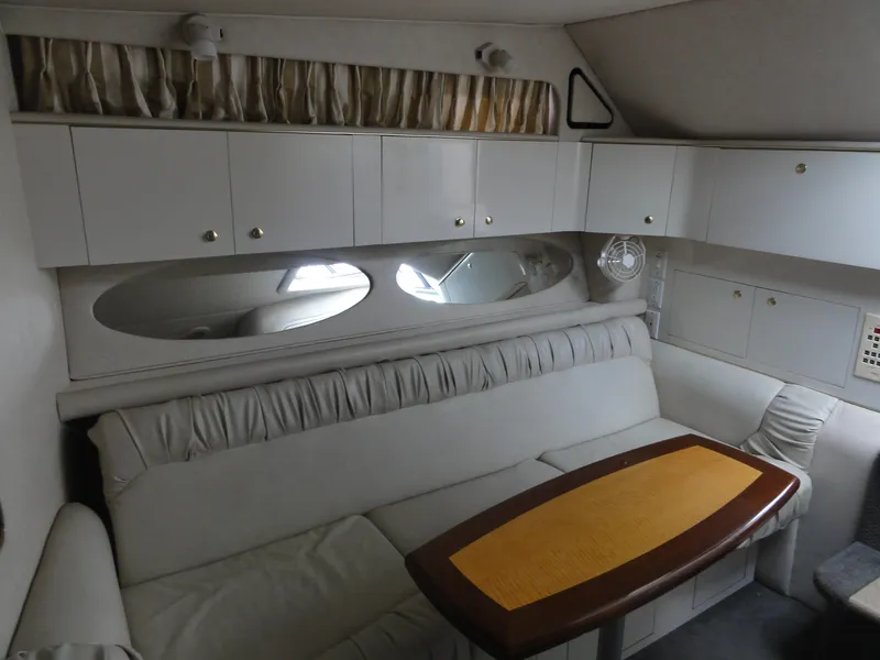 Slide: The Image of 1997 Sea Ray 330 Express cabin interior with white seating, wooden table, and storage cabinets. - 26