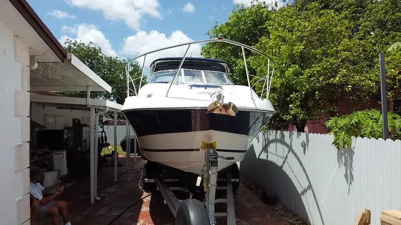 Slide: The Image of 2006 Doral 310 Intrigue boat on trailer, parked in a backyard with trees and a fence. - 13