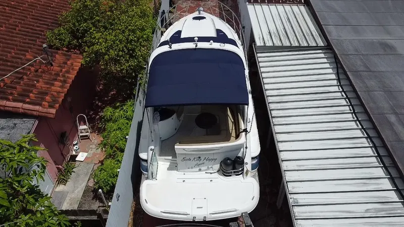 Slide: The Image of 2006 Doral 310 Intrigue boat with blue canopy, parked beside a house. - 3