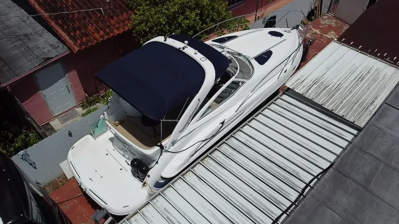 Slide: The Image of 2006 Doral 310 Intrigue boat with blue canopy, parked on a covered driveway. - 4