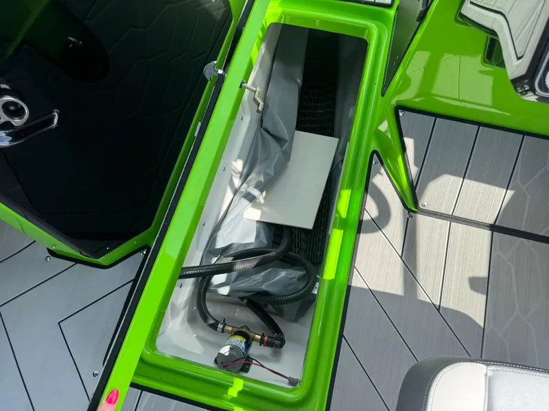 Slide: The Image of 2022 Yamaha Boats 255XD storage compartment with green trim and visible hoses. - 19