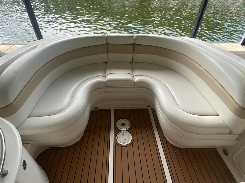 Slide: The Image of 2003 Sea Ray 290 Bowrider interior with curved seating and wooden deck by the water. - 14