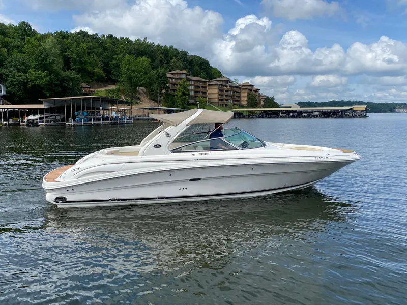 Slide: The Image of 2003 Sea Ray 290 Bowrider cruising on a scenic lake with lush green shoreline. - 4