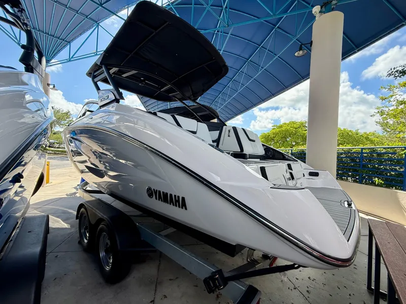 Slide: The Image of 2025 Yamaha Boats 252SD, sleek white design, on trailer under blue canopy. - 3