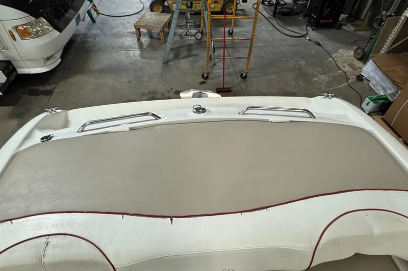 Slide: The Image of 1998 Larson 195 boat interior in a garage setting, featuring beige upholstery and red trim. - 13