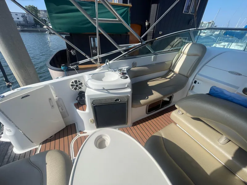 Slide: The Image of 2003 Larson 270 boat interior with seating, table, and mini fridge, docked at marina. - 6